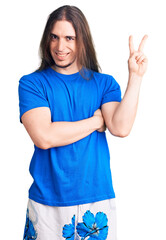 Young adult man with long hair wearing swimwear smiling with happy face winking at the camera doing victory sign. number two.