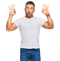 Handsome muscle man wearing casual white tshirt looking surprised and shocked doing ok approval symbol with fingers. crazy expression