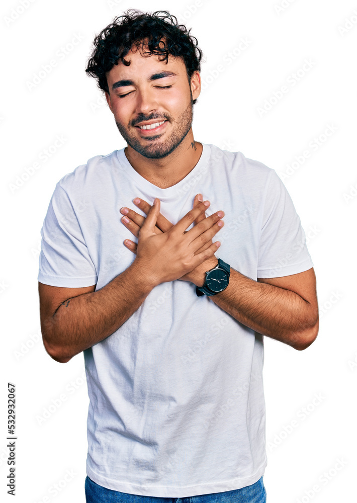 Wall mural Hispanic young man with beard wearing casual white t shirt smiling with hands on chest with closed eyes and grateful gesture on face. health concept.