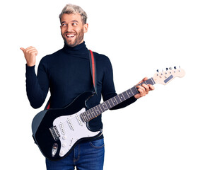 Young handsome blond man playing electric guitar pointing thumb up to the side smiling happy with open mouth