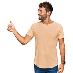 Naklejka premium Handsome young man with beard wearing casual tshirt looking proud, smiling doing thumbs up gesture to the side