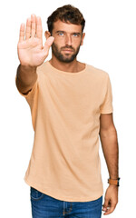 Handsome young man with beard wearing casual tshirt doing stop sing with palm of the hand. warning expression with negative and serious gesture on the face.