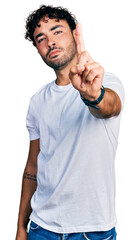 Hispanic young man with beard wearing casual white t shirt pointing with finger up and angry expression, showing no gesture