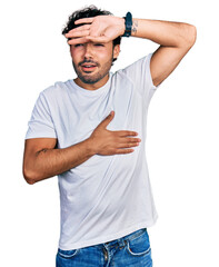 Hispanic young man with beard wearing casual white t shirt touching forehead for illness and fever, flu and cold, virus sick