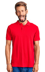 Handsome blond man with beard wearing casual clothes sticking tongue out happy with funny expression. emotion concept.