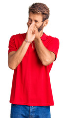 Handsome blond man with beard wearing casual clothes smelling something stinky and disgusting,...