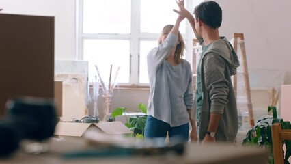 New home, happy couple and moving day while giving high five to celebrate in a house with cardboard boxes for unpacking. Excited man and woman with mortgage or loan loan approval in apartment