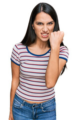 Fototapeta premium Young hispanic girl wearing casual striped t shirt angry and mad raising fist frustrated and furious while shouting with anger. rage and aggressive concept.