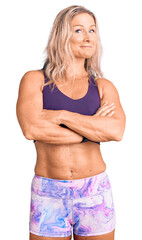 Middle age fit blonde woman wearing sportswear happy face smiling with crossed arms looking at the...