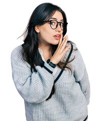 Beautiful hispanic woman wearing casual sweater and glasses hand on mouth telling secret rumor, whispering malicious talk conversation