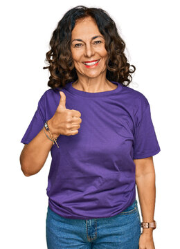 Middle age hispanic woman wearing casual clothes doing happy thumbs up gesture with hand. approving expression looking at the camera showing success.