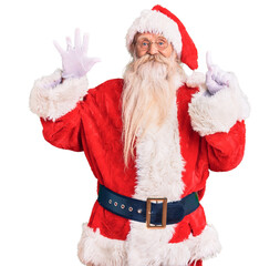 Old senior man with grey hair and long beard wearing traditional santa claus costume showing and pointing up with fingers number six while smiling confident and happy.