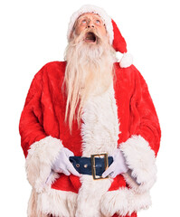 Old senior man with grey hair and long beard wearing traditional santa claus costume angry and mad...