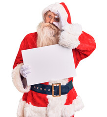 Old senior man with grey hair and long beard wearing santa claus costume holding banner smiling...