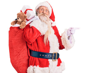 Old senior man with grey hair and long beard wearing santa claus costume holding bag with presents...