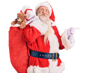 Old senior man with grey hair and long beard wearing santa claus costume holding bag with presents smiling happy pointing with hand and finger to the side