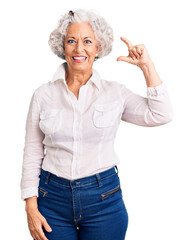 Senior grey-haired woman wearing casual clothes smiling and confident gesturing with hand doing small size sign with fingers looking and the camera. measure concept.