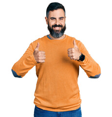 Hispanic man with beard wearing casual winter sweater success sign doing positive gesture with hand, thumbs up smiling and happy. cheerful expression and winner gesture.