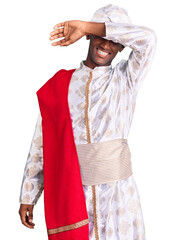 African handsome man wearing tradition sherwani saree clothes covering eyes with arm smiling cheerful and funny. blind concept.