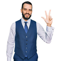 Young man with beard wearing business vest showing and pointing up with fingers number three while smiling confident and happy.