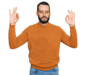 Young man with beard wearing casual winter sweater relax and smiling with eyes closed doing meditation gesture with fingers. yoga concept.