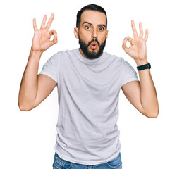 Fototapeta premium Young man with beard wearing casual white t shirt looking surprised and shocked doing ok approval symbol with fingers. crazy expression
