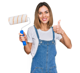Young blonde girl holding roller painter smiling happy and positive, thumb up doing excellent and approval sign