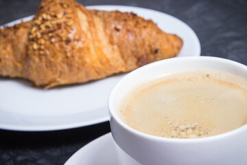 Breakfast consisting of fresh croissant with chocolate and coffee in white cup