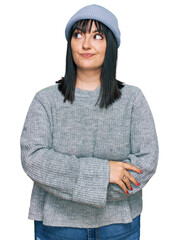 Young hispanic woman wearing cute wool cap smiling looking to the side and staring away thinking.