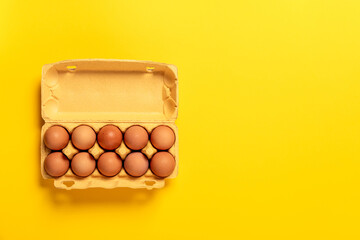 Ten chicken eggs in cardboard package isolated on yellow background. Top view, copy space. Big size XL. Concept of business card grocery store. Fresh eco farm product. Healthy organic food. Banner