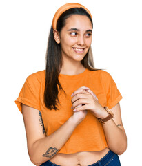 Young hispanic woman wearing casual clothes laughing nervous and excited with hands on chin looking...