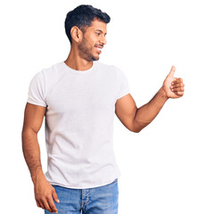 Young latin man wearing casual clothes looking proud, smiling doing thumbs up gesture to the side