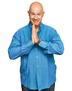 Middle age bald man wearing casual clothes praying with hands together asking for forgiveness smiling confident.
