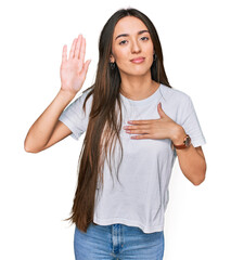 Young hispanic girl wearing casual white t shirt swearing with hand on chest and open palm, making...