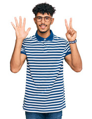 Naklejka premium Young arab man wearing casual clothes and glasses showing and pointing up with fingers number seven while smiling confident and happy.