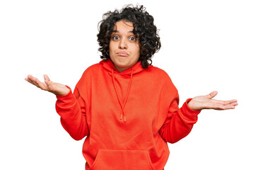 Young hispanic woman with curly hair wearing casual sweatshirt clueless and confused expression...