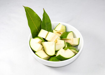 a bowl of raw green mangoes with mango leaves isolated on white background.