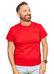 Fototapeta premium Handsome middle age man wearing casual red tshirt looking away to side with smile on face, natural expression. laughing confident.