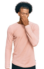 African american man with afro hair wearing casual clothes smelling something stinky and disgusting, intolerable smell, holding breath with fingers on nose. bad smell