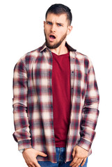 Young handsome man wearing casual shirt in shock face, looking skeptical and sarcastic, surprised with open mouth