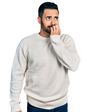 Young hispanic man with beard wearing casual white sweater looking stressed and nervous with hands on mouth biting nails. anxiety problem.