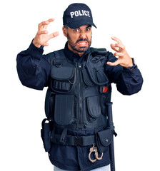 Young hispanic man wearing police uniform shouting frustrated with rage, hands trying to strangle, yelling mad