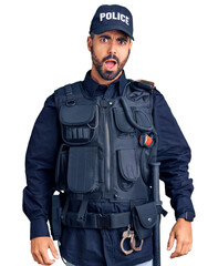 Young hispanic man wearing police uniform in shock face, looking skeptical and sarcastic, surprised...