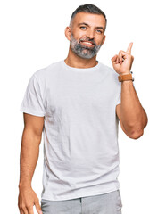 Middle age handsome man wearing casual white tshirt with a big smile on face, pointing with hand finger to the side looking at the camera.