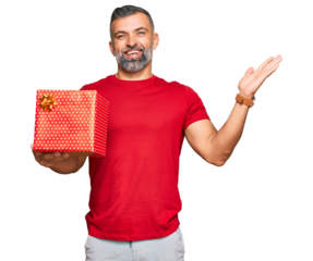Middle age handsome man holding gift celebrating victory with happy smile and winner expression with raised hands