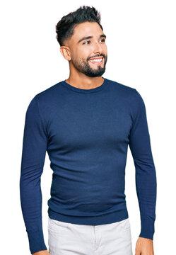 Young man with beard wearing casual blue winter sweater looking away to side with smile on face, natural expression. laughing confident.