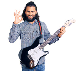 Young arab man playing electric guitar doing ok sign with fingers, smiling friendly gesturing...