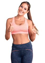 Young beautiful hispanic woman wearing sportswear success sign doing positive gesture with hand, thumbs up smiling and happy. cheerful expression and winner gesture.