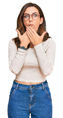 Young brunette woman wearing casual clothes and glasses shocked covering mouth with hands for mistake. secret concept.