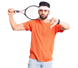 Young handsome man with beard playing tennis holding racket with angry face, negative sign showing dislike with thumbs down, rejection concept